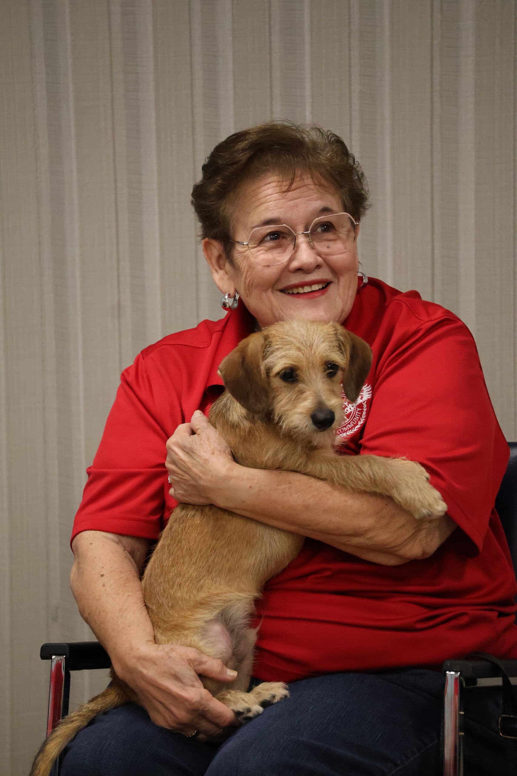 Smiling woman with glasses holding a small dog.