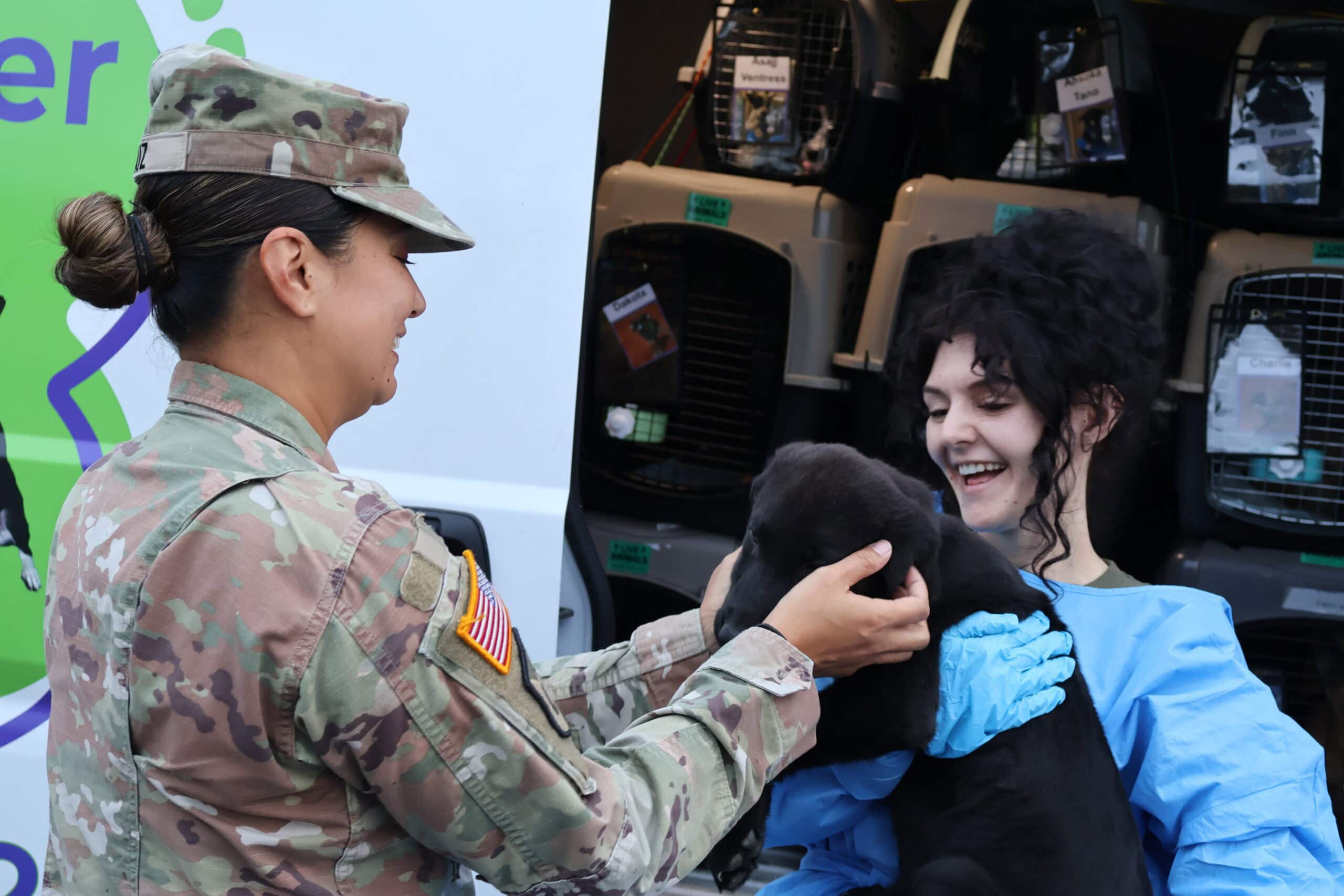 Soldier holds puppy with woman's assistance and smile.