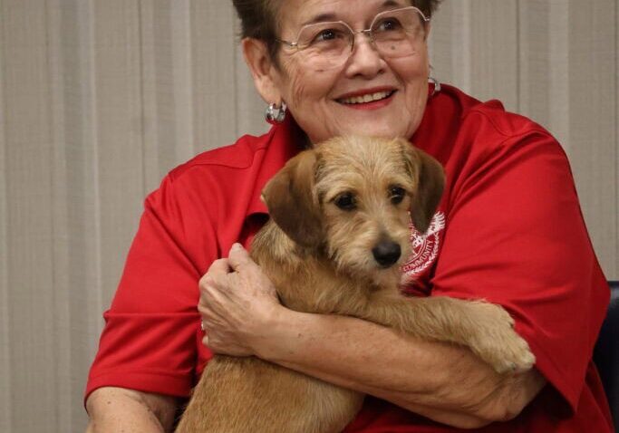 Smiling woman with glasses holding a small dog.