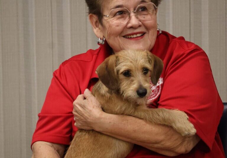 Smiling woman with glasses holding a small dog.